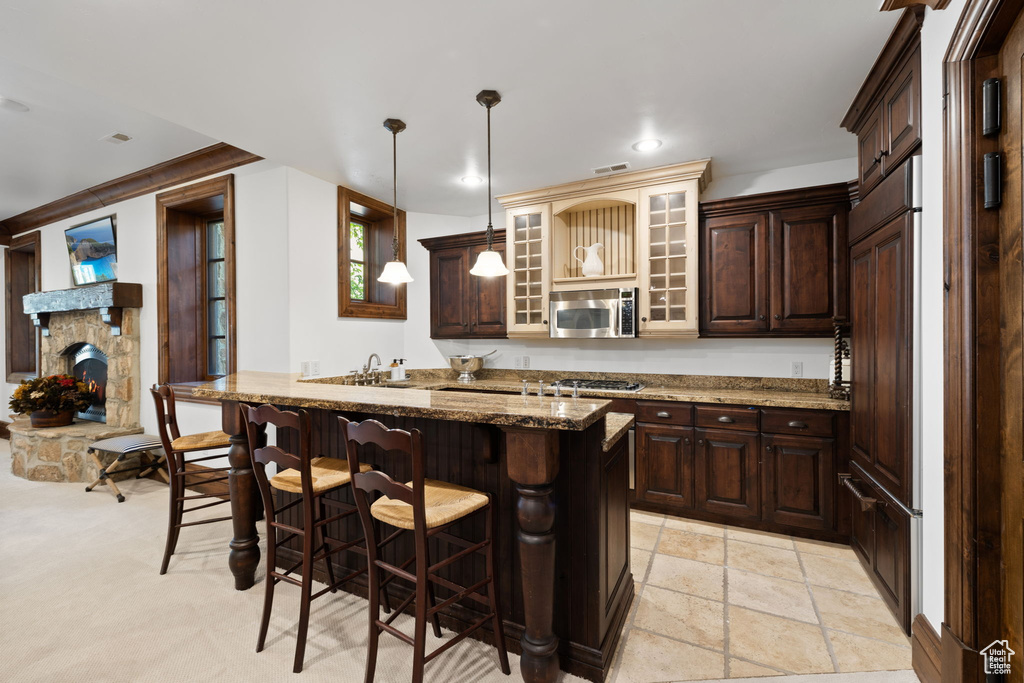 Kitchen featuring recessed lighting, dark brown cabinetry, stainless steel microwave, a kitchen bar, and dark stone counters