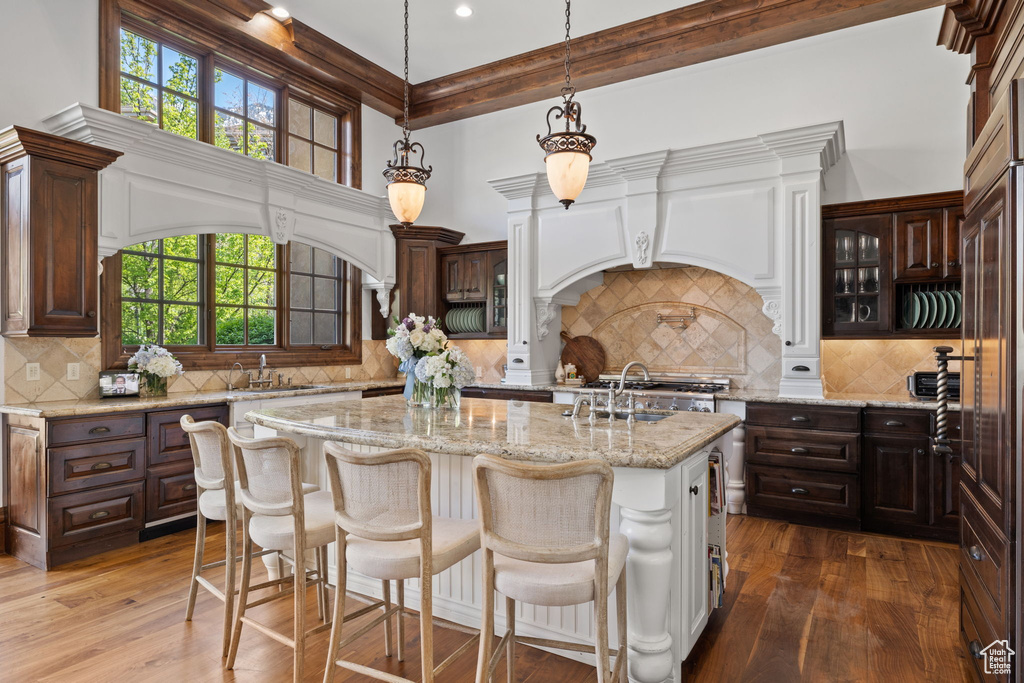 Kitchen with dark brown cabinets, dark wood-style flooring, an island with sink, and decorative backsplash