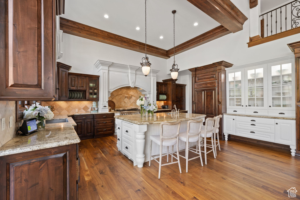 Kitchen featuring a kitchen bar, a kitchen island with sink, white cabinetry, a towering ceiling, and backsplash