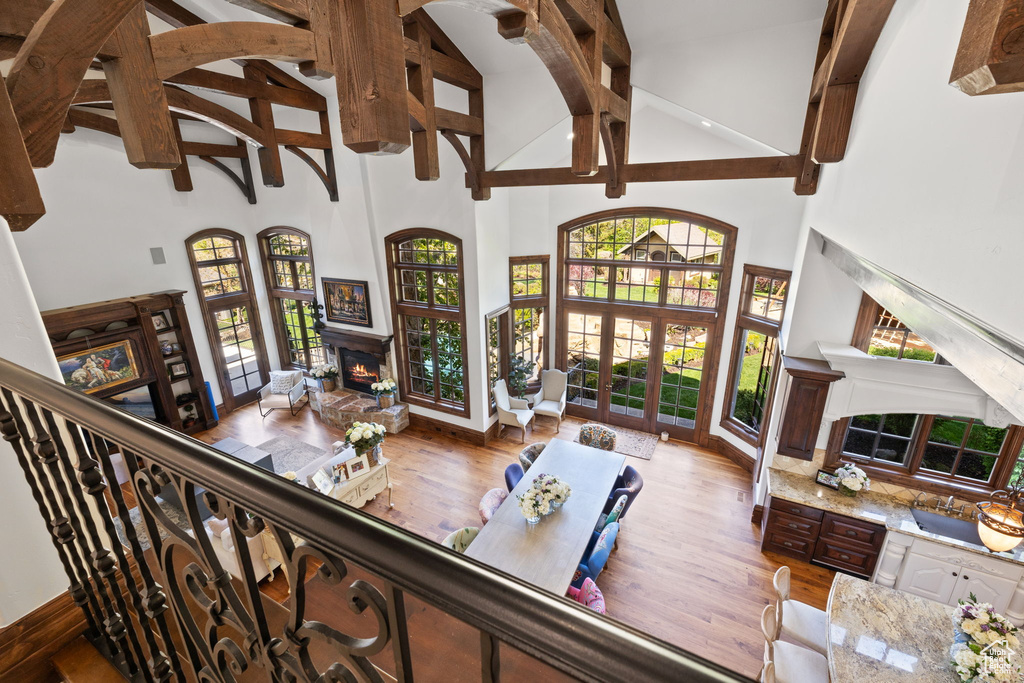 Living room with french doors, wood finished floors, high vaulted ceiling, beam ceiling, and a warm lit fireplace