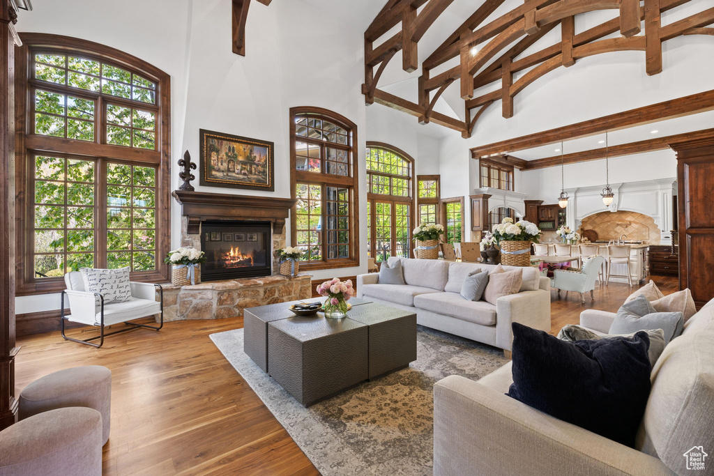 Living room with a wealth of natural light, wood finished floors, a stone fireplace, and high vaulted ceiling