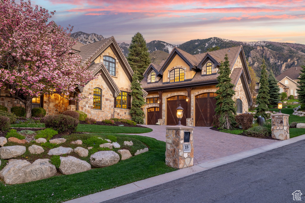 French provincial home featuring a mountain view, stone siding, a yard, driveway, and a garage