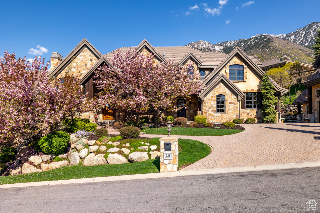 View of front facade with curved driveway, a mountain view, stucco siding, and stone siding