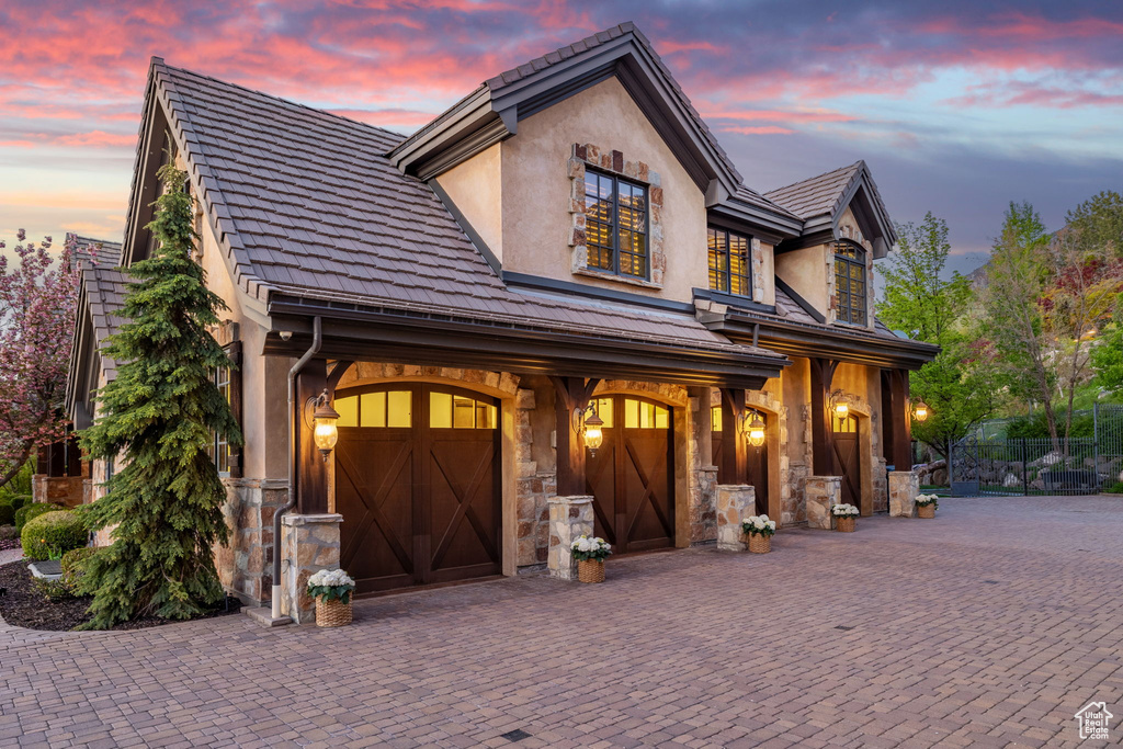 French provincial home with stone siding, stucco siding, driveway, and a garage
