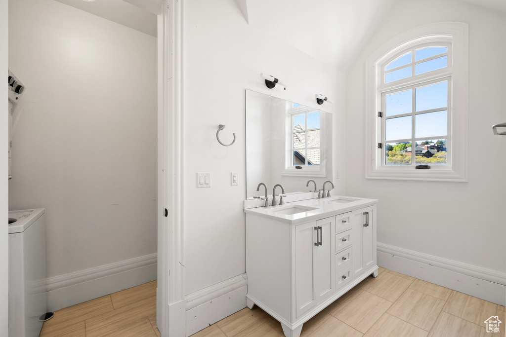 Bathroom with double vanity, vaulted ceiling, baseboards, and a sink