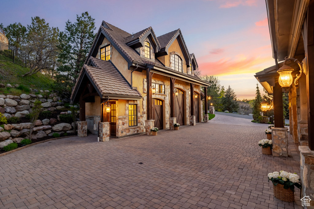 Exterior space with stone siding, a garage, stucco siding, and curved driveway