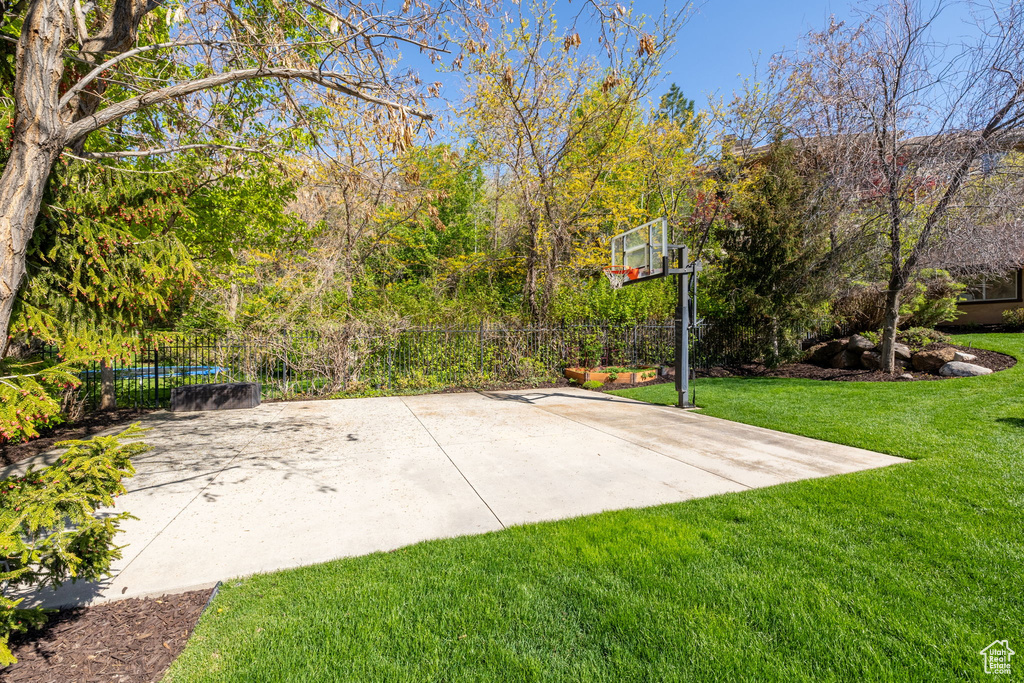 View of sport court with fence, basketball hoop, and a lawn