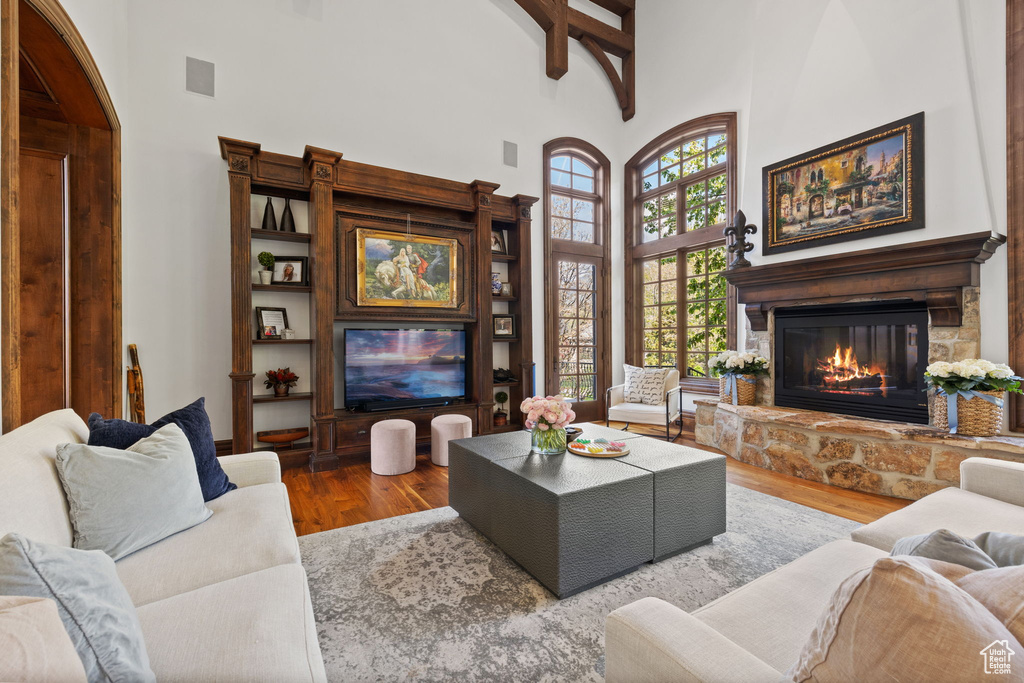 Living area with a stone fireplace, beam ceiling, a towering ceiling, and wood finished floors