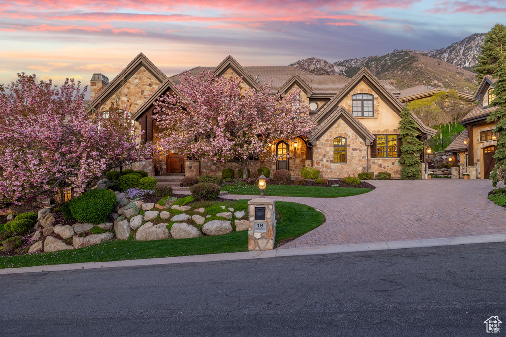 French country home with a lawn, a mountain view, stucco siding, stone siding, and curved driveway