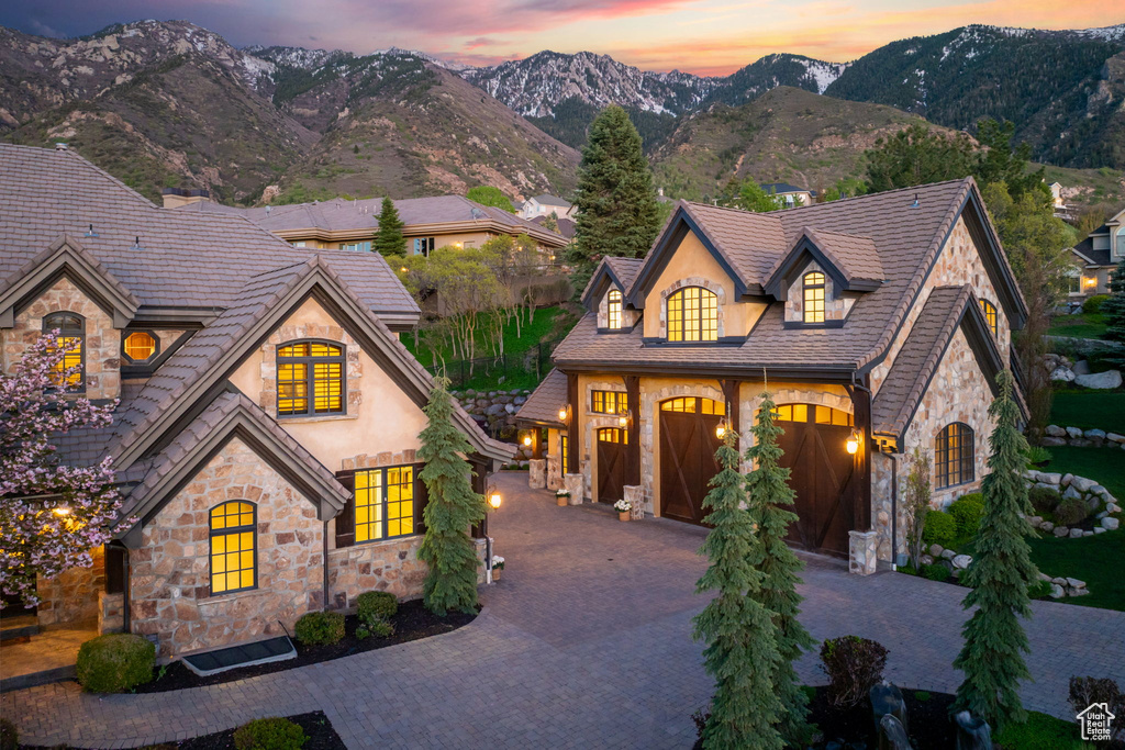 French country inspired facade featuring stone siding, a mountain view, decorative driveway, and stucco siding