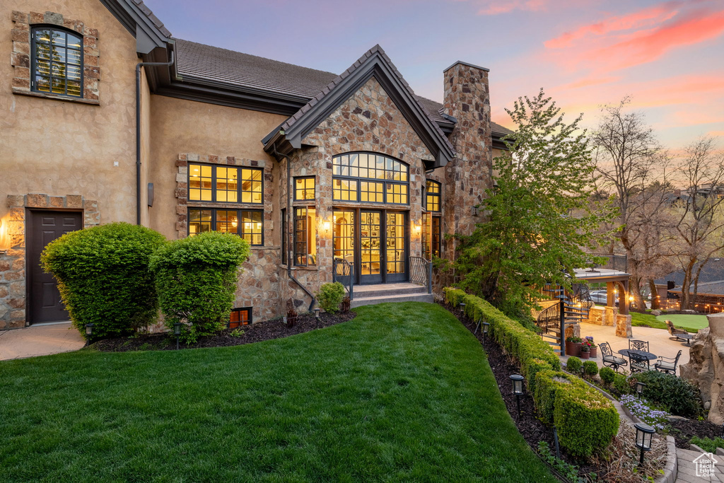 Back of house with a yard, stucco siding, a chimney, and stone siding