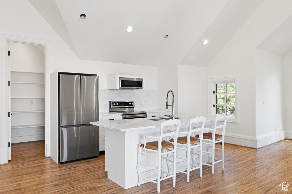 Kitchen featuring lofted ceiling, light wood-style flooring, a sink, a kitchen breakfast bar, and appliances with stainless steel finishes