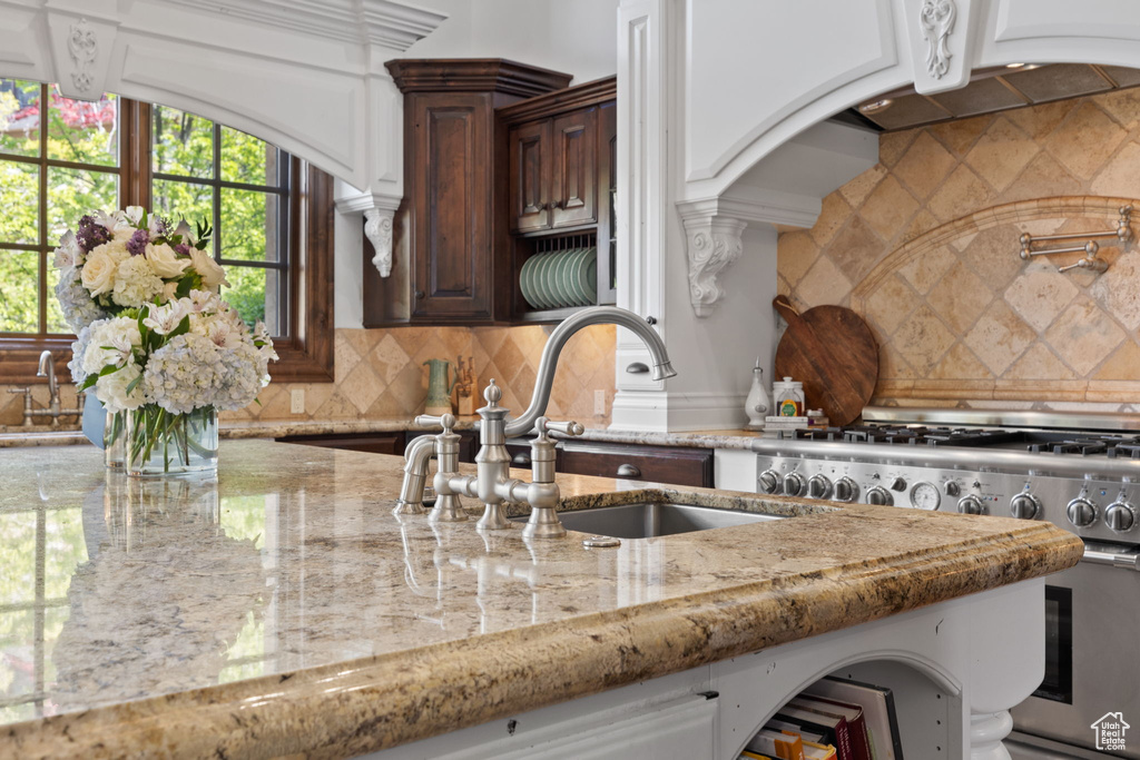 Kitchen featuring a sink, high end stove, decorative backsplash, and light stone counters
