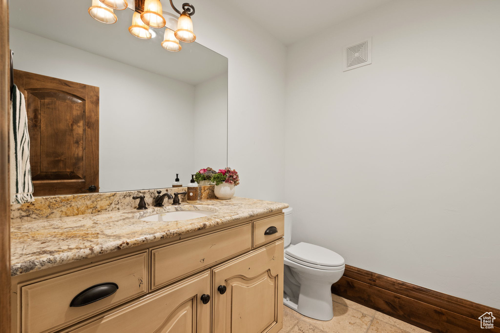 Half bathroom with toilet, baseboards, visible vents, vanity, and a chandelier