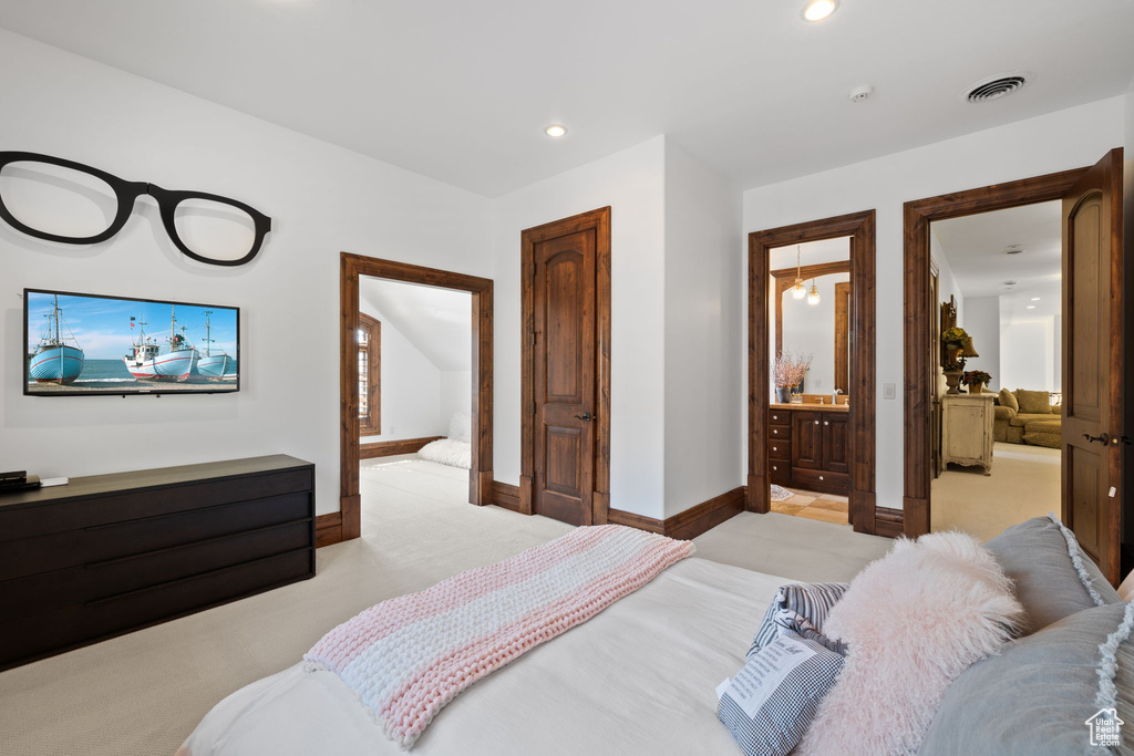 Bedroom with baseboards, ensuite bath, visible vents, and light colored carpet