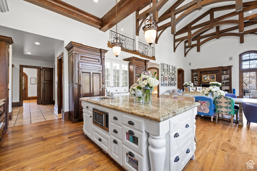Kitchen featuring stainless steel microwave, a sink, light wood-type flooring, high vaulted ceiling, and arched walkways