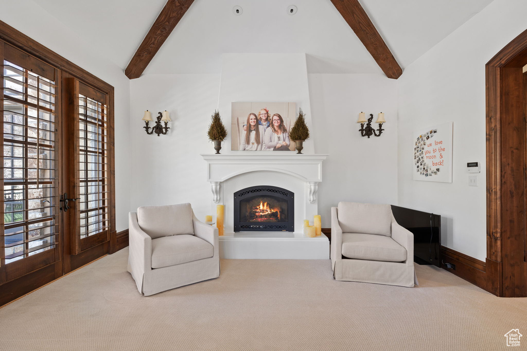 Sitting room featuring a lit fireplace, carpet, and vaulted ceiling with beams