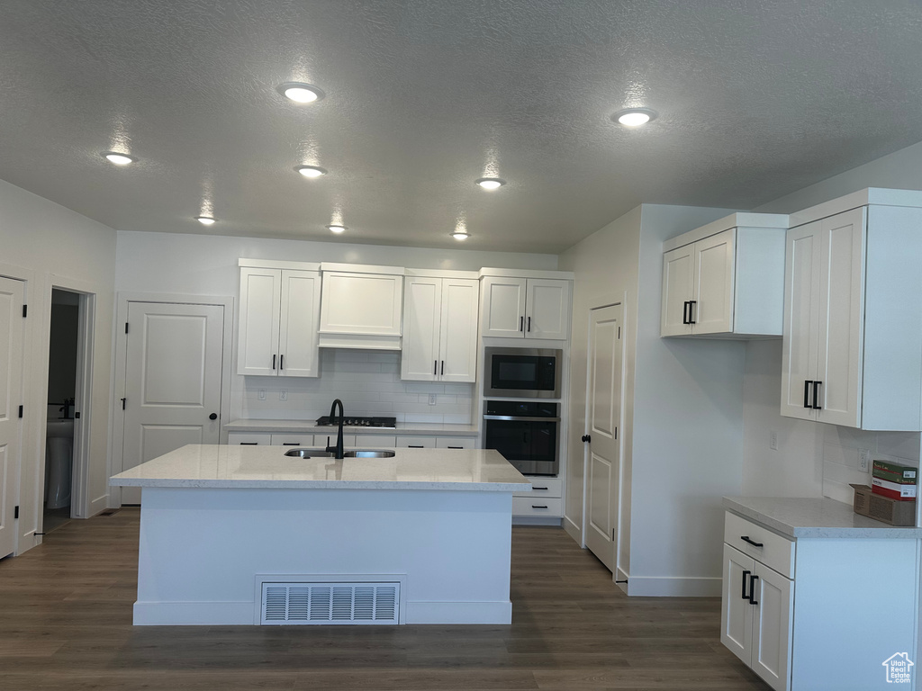 Kitchen featuring stainless steel appliances, dark wood-type flooring, baseboards, decorative backsplash, and a textured ceiling