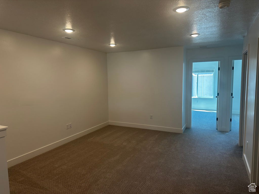 Spare room with dark carpet, baseboards, a textured ceiling, and a smoke detector