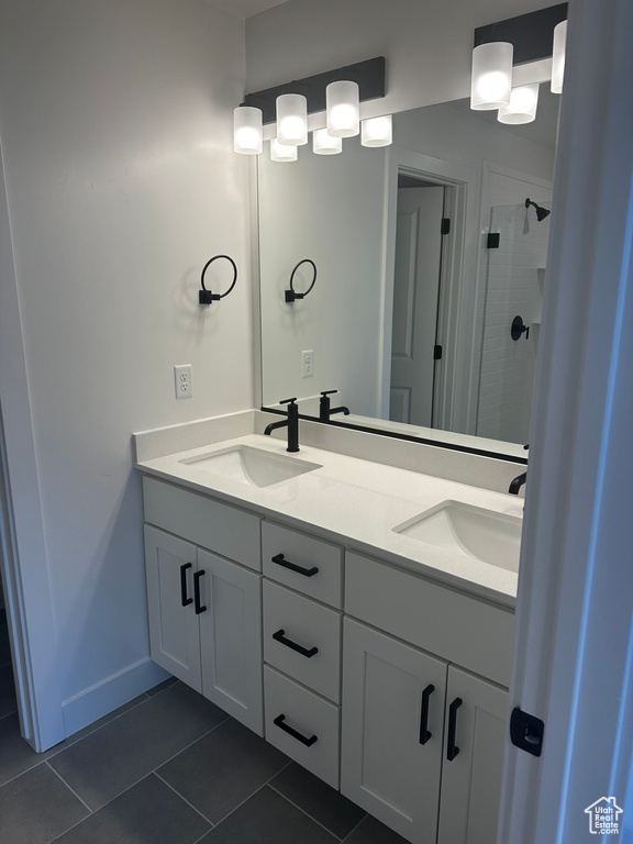 Full bath with tile patterned flooring, a shower stall, double vanity, and baseboards