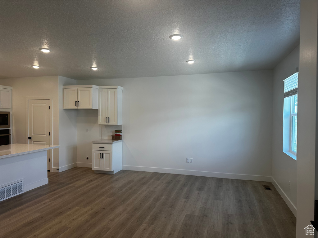 Unfurnished dining area with dark wood finished floors, a textured ceiling, baseboards, and recessed lighting