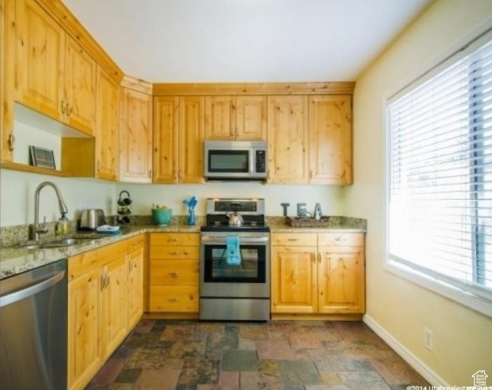 Kitchen with stainless steel appliances, a sink, stone finish flooring, and baseboards