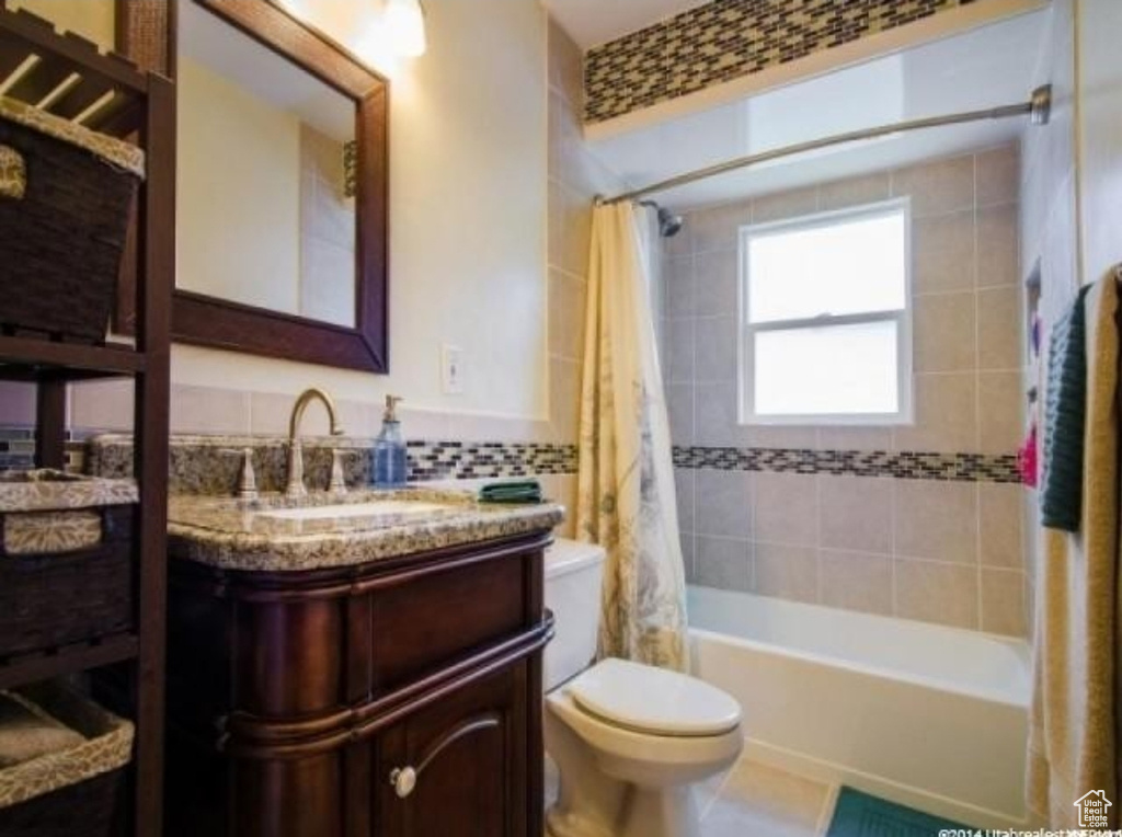 Bathroom featuring toilet, shower / bath combination with curtain, vanity, and decorative backsplash