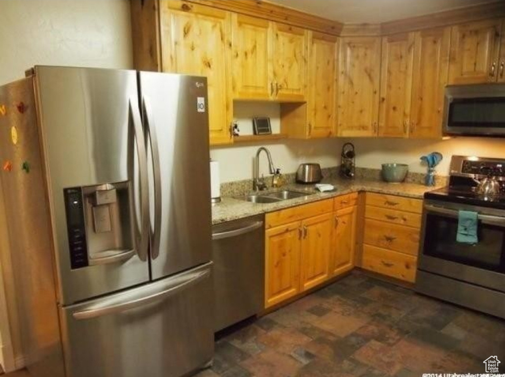 Kitchen with stainless steel appliances, a sink, light stone countertops, and stone finish flooring