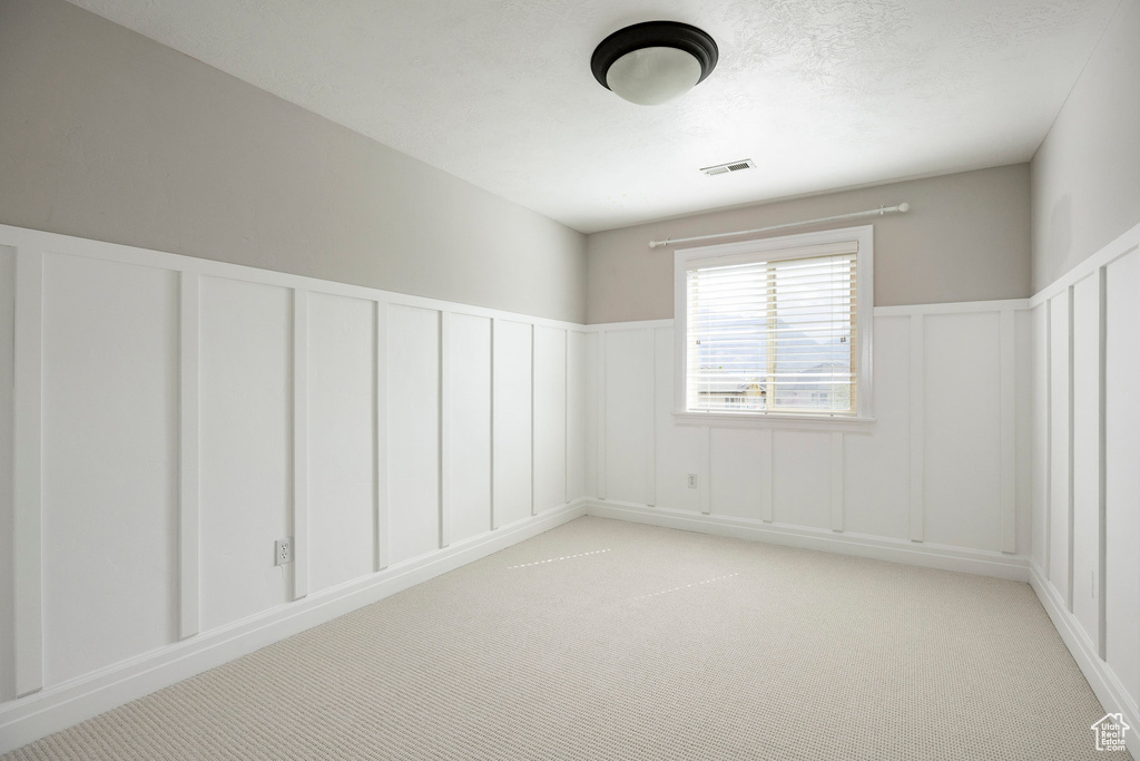 Empty room featuring wainscoting, light colored carpet, a decorative wall, and visible vents