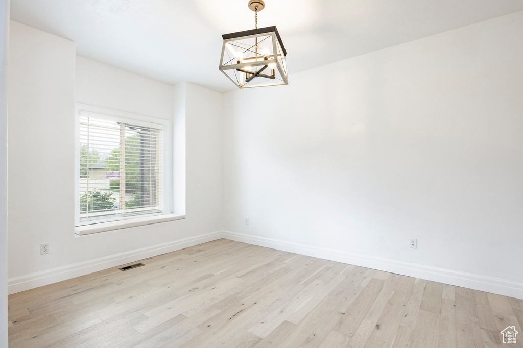 Spare room featuring baseboards, a notable chandelier, light wood finished floors, and visible vents