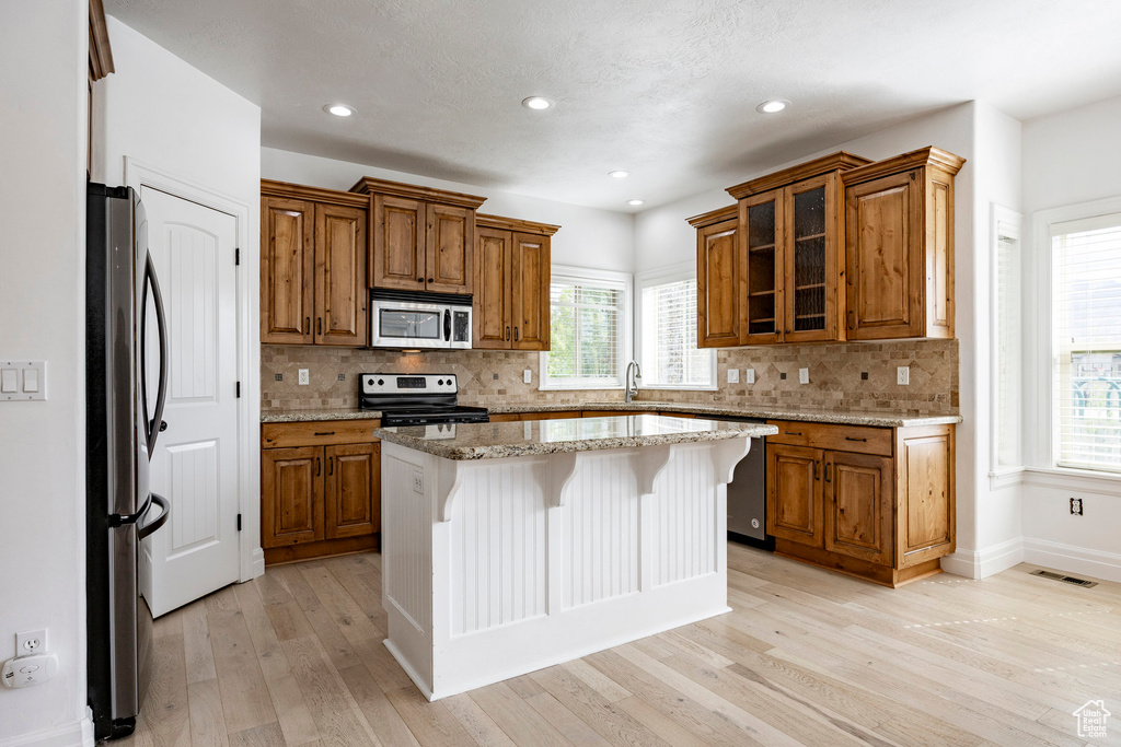 Kitchen featuring appliances with stainless steel finishes, brown cabinets, light wood-style flooring, and a sink