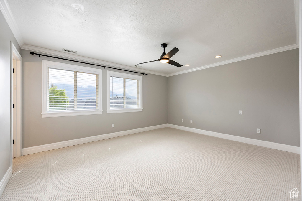 Spare room featuring light colored carpet, visible vents, crown molding, a wealth of natural light, and a ceiling fan