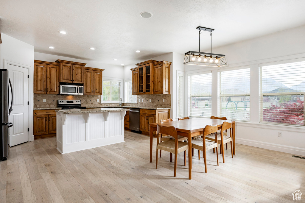Kitchen with stainless steel appliances, tasteful backsplash, brown cabinets, light wood-type flooring, and a kitchen island