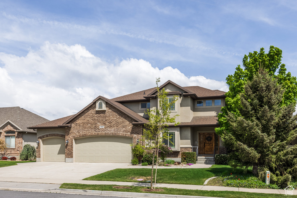 Craftsman-style house featuring stucco siding, concrete driveway, an attached garage, a front lawn, and brick siding