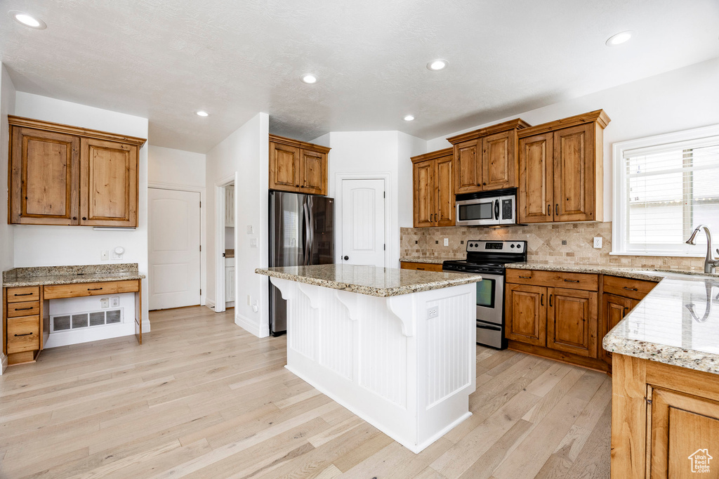 Kitchen with stainless steel appliances, a sink, a kitchen bar, light wood finished floors, and light stone counters