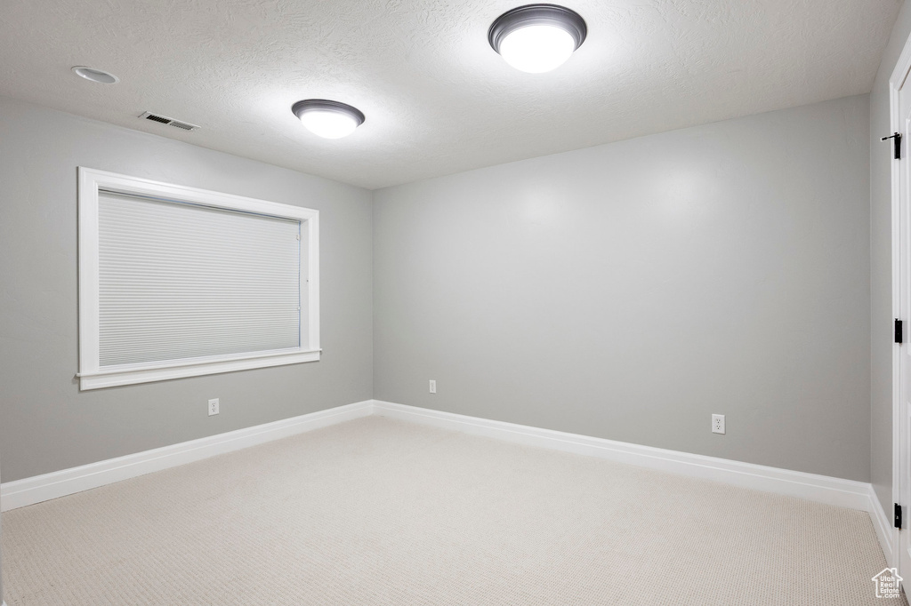 Unfurnished room featuring a textured ceiling, light carpet, baseboards, and visible vents