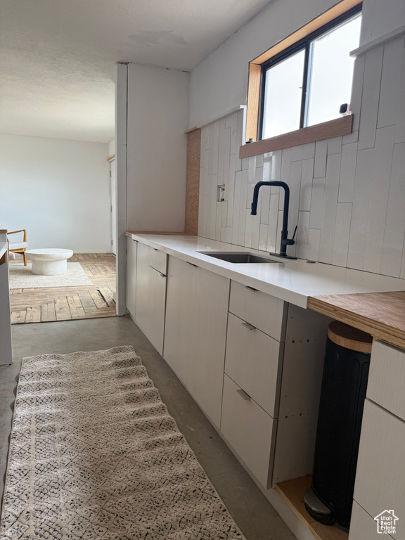 Kitchen featuring a sink, light countertops, concrete floors, and decorative backsplash