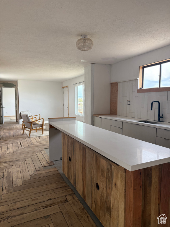 Kitchen featuring a sink, light countertops, plenty of natural light, tasteful backsplash, and a textured ceiling