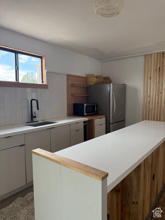Kitchen with appliances with stainless steel finishes, a sink, light countertops, backsplash, and a textured ceiling