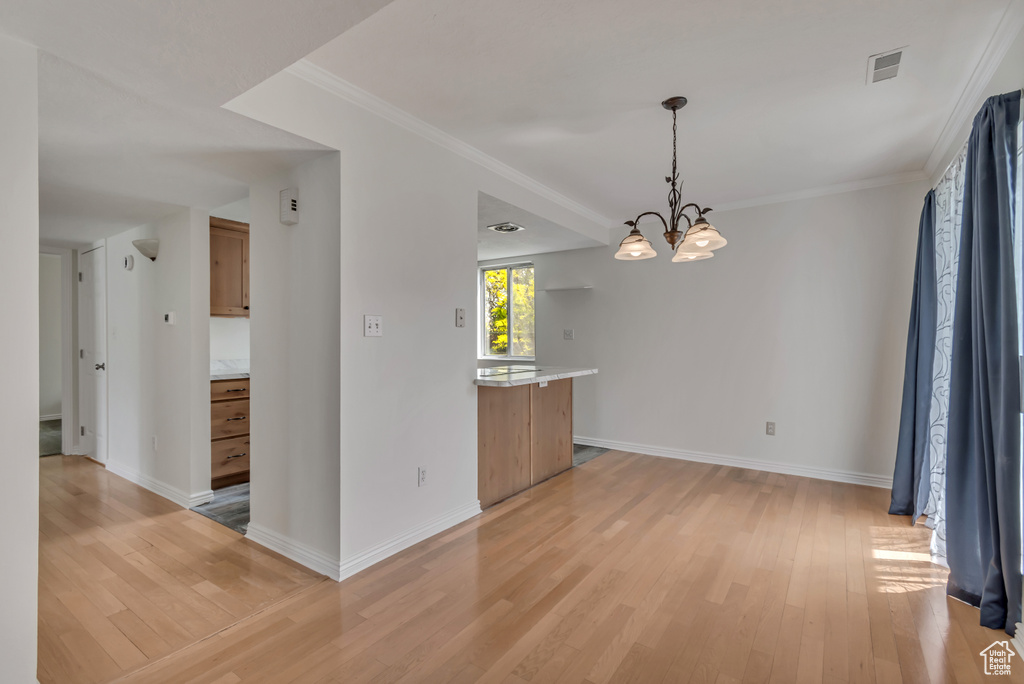 Unfurnished dining area featuring a chandelier, light wood-style floors, baseboards, and ornamental molding