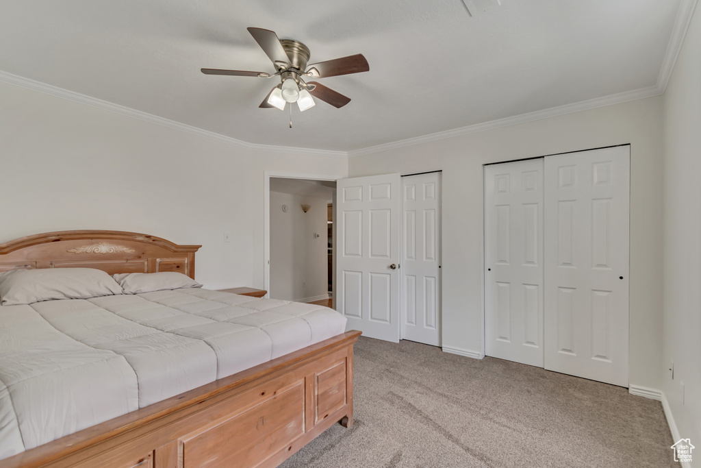 Bedroom with two closets, ornamental molding, light colored carpet, baseboards, and a ceiling fan