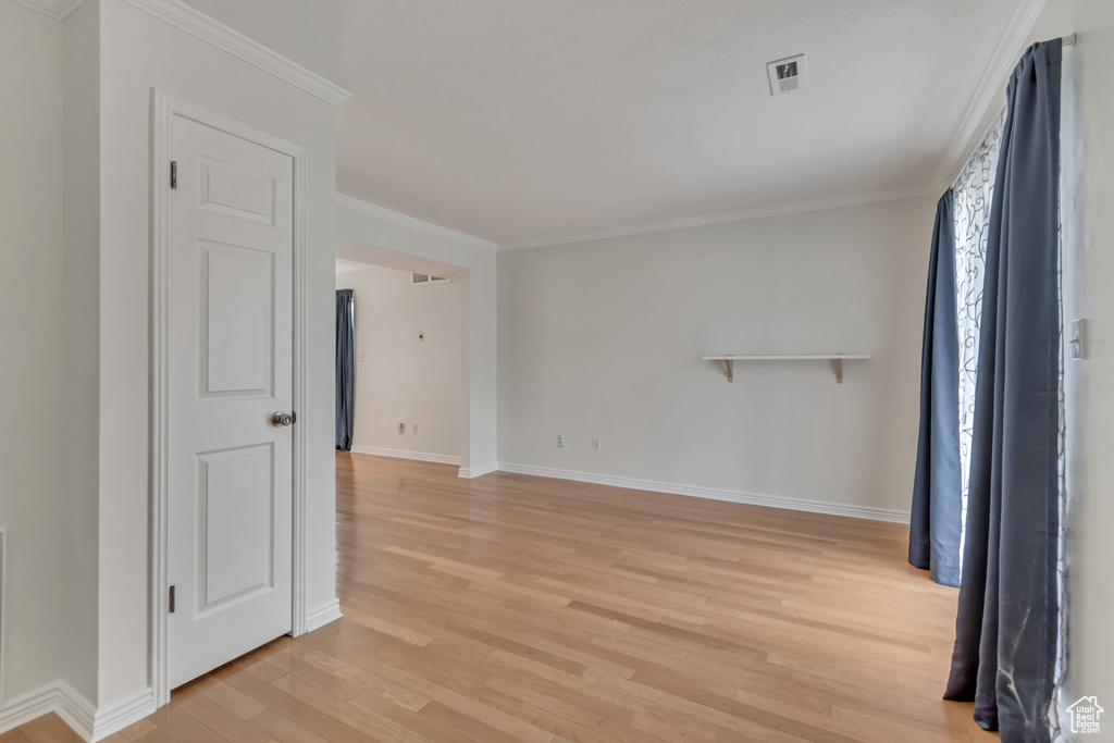 Empty room with light wood-style flooring, baseboards, and crown molding