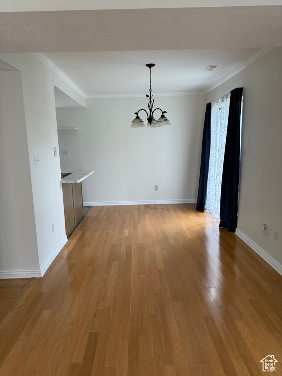 Unfurnished dining area with a chandelier, light wood-type flooring, ornamental molding, and baseboards