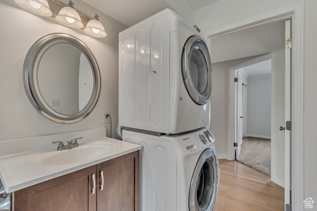 Clothes washing area with estacked washer and dryer, a sink, light wood-type flooring, and baseboards