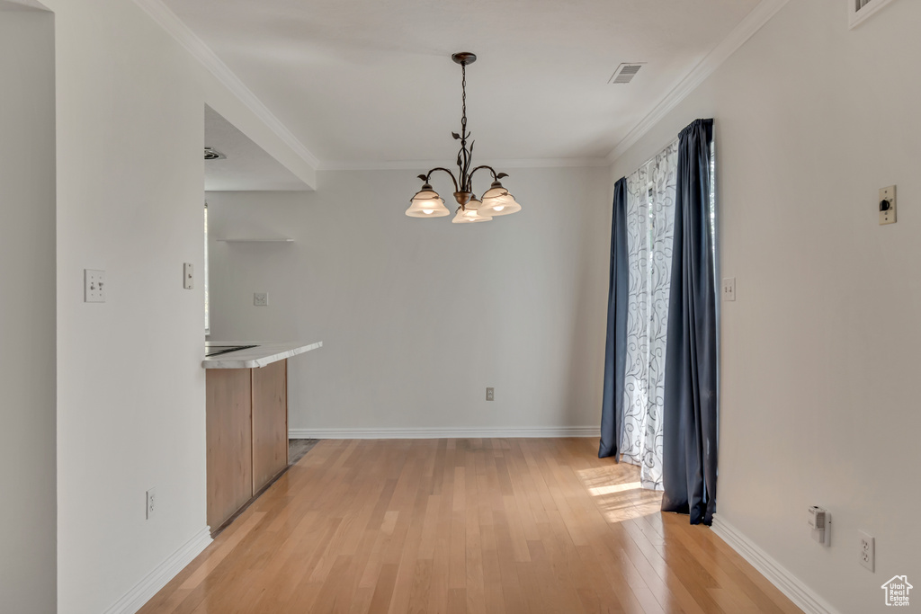 Unfurnished dining area featuring light wood finished floors, a chandelier, baseboards, healthy amount of natural light, and ornamental molding