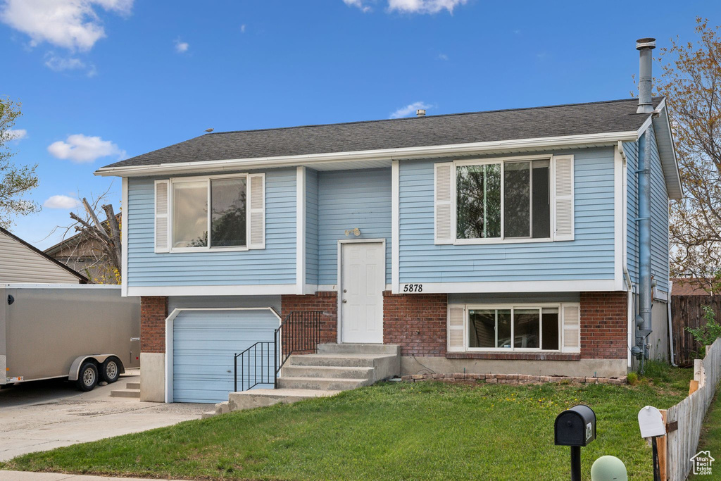 Bi-level home featuring a garage, a front yard, brick siding, and concrete driveway