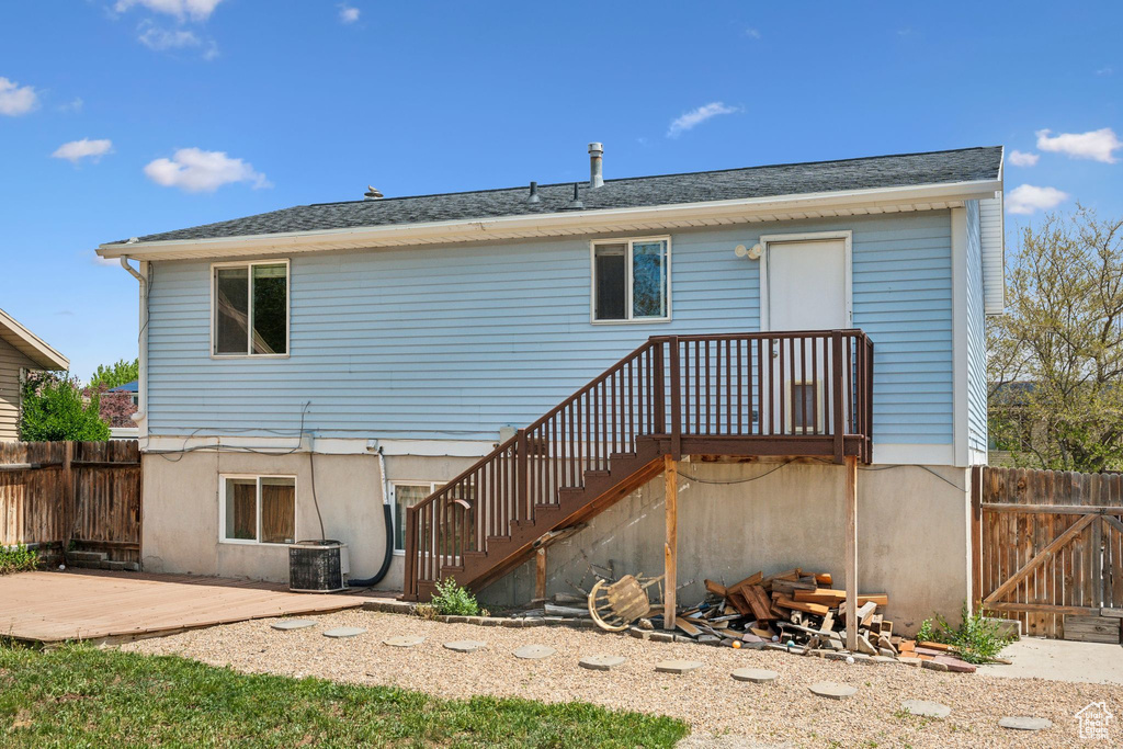 Rear view of property with fence, a wooden deck, central AC unit, stairway, and roof with shingles