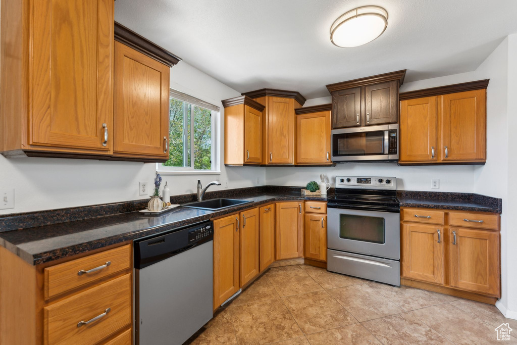 Kitchen with appliances with stainless steel finishes, a sink, brown cabinetry, and dark stone counters