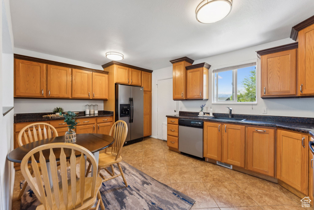 Kitchen featuring appliances with stainless steel finishes, a sink, dark countertops, and brown cabinetry
