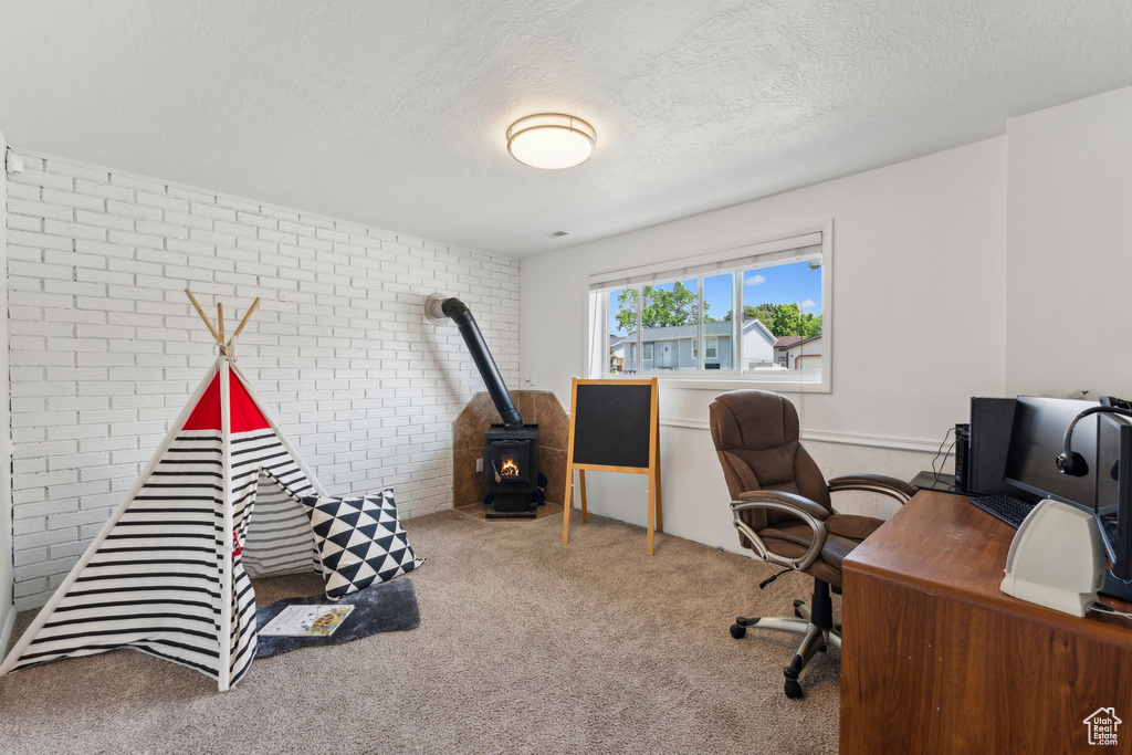 Home office featuring brick wall, a wood stove, a textured ceiling, and carpet floors